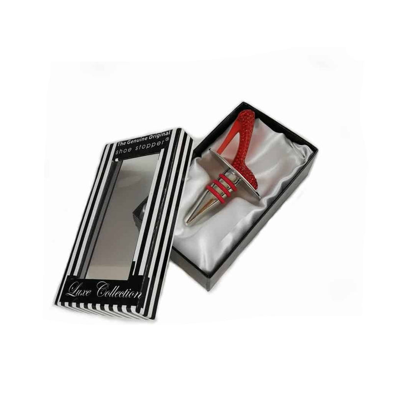 Bottle stopper in the shape of stiletto shoe, covered in red crystals, sitting in gift box which is lined with white satin.  The box is black and white striped and has a clear window on the front to show the shoe wine stopper inside.